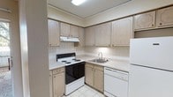 Located at 1201 N Foster Dr in Baton Rouge, Louisiana, this single-floor unit offers a straightforward and functional layout across several well-defined living spaces. The interior is finished in warm neutral tones throughout, creating a cohesive and understated aesthetic.

The kitchen is efficiently designed with light wood cabinetry extending to the upper walls, white laminate countertops, a white tile backsplash, and tile flooring. It is equipped with a coil-burner electric range, a built-in dishwasher, a stainless steel sink, and a refrigerator, with an overhead range hood providing ventilation.

The living area features plush carpeting, track lighting on the ceiling, and a sliding glass door that opens to an outdoor view, allowing natural light to fill the space. A ceiling fan adds comfort to the room, which connects openly to the kitchen area via a partial wall divider.

The bedrooms are carpeted and generously sized, each equipped with ceiling fans and ample closet storage. One bedroom features bifold louvered closet doors with built-in shelving, while another includes sliding panel closet doors with shelving units. Windows in the bedrooms provide natural light and outdoor views.

The bathroom includes a full tub-shower combination, white square tile wainscoting along the walls, a toilet, and tile flooring, presenting a clean and functional design.