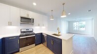 This single-floor residence at Alta Porter On Peachtree in Brookhaven, Georgia, offers a thoughtfully designed open-concept layout with modern finishes throughout. The kitchen serves as a central highlight, featuring a striking two-tone cabinet design with navy lower cabinets and crisp white upper cabinets, all accented by gold hardware. White quartz countertops extend across the peninsula, which includes an undermount sink with a gold faucet and is illuminated by stylish pendant lighting. Stainless steel appliances, including a gas range, microwave, dishwasher, and refrigerator, complete the well-equipped space. A white subway tile backsplash adds a clean, polished touch.

The living area flows seamlessly from the kitchen, featuring light hardwood-style flooring and a ceiling fan that enhances the bright, airy atmosphere. A large window allows natural light to fill the space, creating an inviting ambiance. In-unit stacked laundry is conveniently accessible near the main living area.

The bathroom features a glass-enclosed walk-in shower with large white tiles and matte black hardware, complemented by light wood-style flooring. A generously sized walk-in closet with wire shelving and carpeted flooring provides ample storage. The overall design palette of soft whites, natural wood tones, and gold and black accents gives the space a cohesive, contemporary aesthetic.