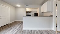 This single-floor unit offers a thoughtfully designed layout that maximizes its compact footprint. Wood-style luxury vinyl plank flooring runs throughout, lending a cohesive, contemporary feel to every room. The neutral gray and white color palette creates a clean, bright atmosphere that enhances the sense of space.

The open living area connects seamlessly to the kitchen via a peninsula with granite countertops, providing both a functional workspace and a natural divider between the two areas. The kitchen features white cabinetry, black appliances including a refrigerator, electric range, and under-cabinet range hood, along with a stainless steel sink. Upper cabinets extend on both sides of the kitchen, offering ample storage.

The bedroom is bright and airy, benefiting from a window fitted with horizontal blinds that allow for adjustable natural light. Its clean walls and generous floor space provide a comfortable, versatile retreat.

The bathroom maintains the same consistent aesthetic, with wood-style flooring, a white vanity topped with granite countertops, a white toilet, and textured walls. Brushed nickel hardware and a towel bar add polished finishing touches throughout the space.