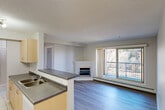 Located at 10411 105 Avenue NW in Edmonton, Alberta, this well-appointed two-bedroom, two-bathroom unit offers a functional and comfortable single-floor layout. The open-concept living and dining area is a highlight, featuring durable hardwood-style flooring, a textured ceiling, and a corner fireplace that adds warmth and character. Large sliding glass doors flood the space with natural light and open onto a private balcony with scenic views of surrounding trees, creating a pleasant indoor-outdoor connection. The galley-style kitchen is efficiently designed with light maple cabinetry, grey laminate countertops, a classic white subway tile backsplash, a double-basin sink, and a full suite of white appliances, including a stove, refrigerator, and microwave. Tile flooring completes the kitchen's clean, practical aesthetic. The spacious primary bedroom features a window with a natural view, mirrored sliding closet doors, and light hardwood-style flooring. A central hallway connects the rooms, with three closets providing ample storage throughout. Both bathrooms are finished with light maple vanities, grey countertops, and tile flooring, with one featuring a standalone glass-door shower. A dedicated in-unit laundry space with a stacked washer and dryer adds everyday convenience to this well-rounded home.