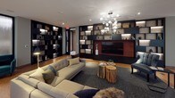 This elegantly designed single-floor space offers a refined and cohesive lounge environment that blends contemporary aesthetics with warm, natural materials. The distinctive cork flooring runs throughout, providing both visual warmth and a unique textural quality underfoot. Floor-to-ceiling windows with sheer roller shades line multiple walls, allowing abundant natural light to permeate the interior while maintaining a soft, diffused ambiance.

The space is organized into distinct seating zones, each thoughtfully curated. One area features a generous sectional sofa in neutral tones, accented with decorative pillows and anchored by a dark area rug. Natural wood stump side tables add an organic touch. A second lounge zone showcases tan leather sofas arranged around a glass coffee table, bathed in light from the expansive corner windows.

A dramatic built-in shelving wall, finished in dark tones with integrated lighting, serves as both a functional and decorative focal point. It frames a large flat-screen television and displays curated décor and books. A contemporary globe chandelier adds a striking overhead accent.

A long corridor lined with additional illuminated built-in shelving and glass-fronted rooms connects the various zones, reinforcing the space's open, flowing layout. The overall atmosphere is sophisticated, calm, and well-appointed.