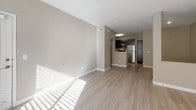 This single-floor residence offers a clean, modern aesthetic throughout, combining practical design with comfortable living spaces. The open-concept living and dining area is finished with light wood-look flooring and neutral warm-beige walls, allowing natural light to pour in through large windows fitted with white horizontal blinds. A ceiling fan adds both style and function to the main living space, which flows seamlessly toward the kitchen. The kitchen is a standout feature, equipped with rich dark espresso cabinetry extending to the ceiling for ample storage, crisp white countertops, and a full suite of stainless steel appliances including a dishwasher, range, and built-in microwave. The bedroom is finished with plush wall-to-wall carpet and features a window that brings in natural light, creating a calm and restful environment. The bathroom includes a full soaking tub with a curved shower rod and overhead shower, complemented by dark cabinetry that mirrors the kitchen's design language. A dedicated in-unit laundry area houses a full-size washer and dryer with overhead wire shelving for additional storage. Throughout the space, white trim and consistent neutral tones create a cohesive, move-in-ready atmosphere.