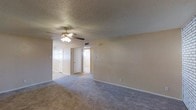This single-story space in Waco, Texas offers a straightforward and functional layout with a calm, neutral aesthetic throughout. The main living area is finished with wall-to-wall carpet in a warm beige tone, contributing to a comfortable and quiet atmosphere underfoot. A ceiling fan with an integrated light fixture is centrally mounted beneath a textured popcorn ceiling, providing both air circulation and ambient lighting to the space.

The walls are painted in a soft, neutral beige that carries consistently throughout the visible areas, lending a cohesive and understated character to the interior. Multiple doorways visible from the main living area lead to additional rooms, suggesting a connected and accessible floor plan. One doorway opens to what appears to be a hallway or secondary room with natural light filtering through, while a closet door is also visible nearby.

Electrical outlets and light switches are positioned at standard heights along the walls, and a ceiling vent indicates a central HVAC system. The overall ambiance is clean, neutral, and move-in ready, offering a blank canvas well-suited for personalization. The single-floor layout ensures ease of navigation throughout the space.