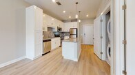 Located in Henrico, Virginia, this single-floor residence offers a thoughtfully designed layout with modern finishes throughout. The kitchen serves as the heart of the space, showcasing crisp white shaker cabinetry, a subtle tile backsplash, and a granite-topped island with pendant lighting overhead. A full suite of stainless steel appliances — including a range, microwave, dishwasher, and refrigerator — completes the kitchen's functional and stylish appeal. Light-toned hardwood flooring runs throughout the main living areas, lending warmth and continuity to the open layout. The living area benefits from large windows that draw in generous natural light and connect to a ceiling fan, creating a bright and comfortable atmosphere. A dedicated hallway leads to the private areas of the home, including a well-appointed bathroom featuring marble-style tile flooring, a granite vanity with white cabinetry, and a full tub-shower combination. The bedroom is spacious with clean neutral walls and the same hardwood flooring, offering a versatile canvas. The unit's overall aesthetic is clean and contemporary, with consistent use of granite, white cabinetry, and brushed hardware tying each space together cohesively.
