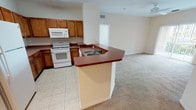 Located at 8100 Claire Ann Drive in Orlando, Florida, this single-floor unit offers a practical and well-organized layout designed for comfortable everyday living. The open-concept kitchen is a central highlight, featuring warm-toned wooden cabinetry, a full suite of white appliances including a refrigerator, electric range, and built-in microwave, and a wraparound peninsula with a rich dark countertop that provides ample workspace and casual dining space. Light tile flooring runs throughout the kitchen, transitioning to plush wall-to-wall carpeting in the living and bedroom areas. The living area is bright and open, benefiting from natural light and ceiling fan fixtures that promote airflow. The bedrooms are generously sized, each offering large windows with exterior views, neutral toned walls, and soft carpeted floors. Two full bathrooms serve the unit — one featuring a soaking tub with a tiled surround and shower combination, and another with a standard tub-shower setup. A dedicated laundry area with washer and dryer hookups adds a layer of convenience. Track lighting in the living space and consistent neutral finishes throughout lend the unit a clean, cohesive aesthetic.
