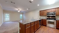 This two-story home is thoughtfully laid out across two levels connected by a carpeted staircase with dual handrails. The main level centers around an open-concept kitchen and living area. The kitchen is well-appointed with rich medium-toned wood cabinetry, granite-style countertops, stainless steel appliances including a range, built-in microwave, and refrigerator, plus a dishwasher. A central island with an integrated double sink and additional cabinetry extends toward the adjoining living area, which features hardwood-style flooring that transitions to carpet. Crown molding, recessed lighting, and a ceiling fan add polish to the shared space, which benefits from natural light through a window. An attached garage with an automatic opener and interior access door provides convenient entry. Upstairs, the primary suite is generously proportioned, featuring plush carpet, a ceiling fan, and multiple windows. The en-suite bath offers a dual-sink vanity with ample cabinetry, tile flooring, and direct access to a walk-in closet with built-in shelving. Additional carpeted rooms provide flexible living space throughout the upper level.