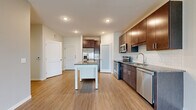 This single-floor unit offers a thoughtfully designed layout with modern finishes throughout. The kitchen serves as a central highlight, showcasing rich dark-brown cabinetry, granite countertops, and a classic white subway tile backsplash. Stainless steel appliances — including a French door refrigerator, electric range, built-in microwave, and dishwasher — provide a complete and functional cooking space. A freestanding island with a granite top and built-in shelving adds additional prep and storage space. A frosted-glass interior door adds a stylish architectural detail near the kitchen area.

The open living area features light wood-style flooring and a sliding glass door that frames views of a green lawn and the surrounding neighborhood, filling the room with natural light. The neutral wall tones throughout create a clean, cohesive aesthetic.

The bedrooms are finished with soft wall-to-wall carpeting, ceiling fans, and windows that offer outdoor views, along with closet access. The bathroom is well-equipped with a dark-wood vanity topped with granite, a tub-shower combination, and light wood-style flooring, completing the unit's consistent design palette.