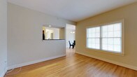This end unit is a single-story residence offering a well-connected, open layout that maximizes its generous square footage. The living area features warm hardwood flooring and neutral-toned walls, creating a bright and inviting atmosphere. A large window with blinds allows natural light to fill the space, enhancing the airy feel throughout.

A pass-through window connects the living area to the kitchen, providing visual openness while maintaining a defined sense of separation between spaces. The kitchen, visible through the pass-through, includes recessed lighting and ample cabinetry. Adjacent to the kitchen, a dedicated dining area is accented by a classic chandelier, offering an elegant setting for meals.

The flow between the living, dining, and kitchen areas makes the layout practical and easy to navigate. With 1.5 bathrooms, the unit is well-suited for daily living and entertaining. As an end unit, it benefits from additional privacy and potentially more natural light from multiple exposures. The consistent hardwood flooring and cohesive neutral palette throughout contribute to a clean, polished aesthetic.