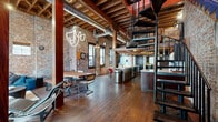 Located at 3722 Walnut St in Denver, CO, this distinctive three-story property masterfully blends industrial character with modern comfort. The main level commands attention with soaring exposed-beam ceilings, original brick walls, polished hardwood floors, and visible ductwork that celebrate the building's raw architectural bones. A dramatic spiral staircase serves as a sculptural centerpiece, connecting the main living and dining areas to an upper loft level. The open-plan kitchen features stainless steel appliances, dark cabinetry with stone countertops, a mosaic tile backsplash, and track lighting beneath warm wooden beams. Two living areas offer flexible lounging and entertaining spaces, each accented by the ever-present exposed brick. The four bedrooms provide a calm retreat from the industrial aesthetic, with clean white walls, large windows offering urban Denver views, and ample natural light. The four bathrooms are finished with dark slate tile, sleek black cabinetry, and marble-topped vanities. A loft adds additional versatile living space on the uppermost level. Two closets and two staircases—including the signature spiral—complete this thoughtfully designed, character-rich urban property.