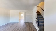 Located in Severn, Maryland, this two-story home offers a functional and well-maintained layout across two floors. The main level features a welcoming living room with a paneled front door, vertical blinds, and durable luxury vinyl plank flooring that extends throughout the home. A carpeted staircase with a black metal railing leads to the upper level. The kitchen is efficiently designed with dark espresso cabinetry, granite-look countertops, a gas range, built-in microwave, and a stainless sink — with the added convenience of a stacked washer and dryer unit tucked neatly into the space. Natural light filters in through a sliding glass door adjacent to the kitchen. Upstairs, three bedrooms offer clean, neutral walls and LVP flooring, each with windows that bring in natural light and outdoor views of the surrounding greenery. The spacious primary bedroom includes a double-door closet. The full bathroom features a tiled shower-tub combo with a window for ventilation and natural light. A hallway connects the upstairs rooms, completing a straightforward and practical floor plan suited for everyday living.