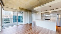 Located on the 16th floor in the heart of Seattle, this modern 2-bedroom, 2-bathroom residence offers a thoughtfully designed layout across a single level. The open living area is a standout, featuring floor-to-ceiling glass windows and an exposed concrete ceiling that lend an industrial-chic aesthetic, while hardwood flooring and abundant natural light create a warm, inviting ambiance. Sweeping views of the downtown Seattle skyline and surrounding urban landscape are visible from multiple vantage points throughout the space.

The contemporary kitchen is well-appointed with stainless steel appliances including a gas range, microwave, and refrigerator. Sleek, light wood cabinetry, a subway tile backsplash, a large island with an undermount sink, and track lighting complete the polished look, all set atop warm hardwood floors.

The primary bedroom features carpeted flooring, exposed concrete ceiling details, and a window with city views, while the second bedroom offers corner windows overlooking the Seattle skyline. A spacious walk-in closet with wire shelving provides generous storage. Both bathrooms are finished with large-format tile, with the primary bath offering a wide vanity, ample cabinetry, and a soaking tub with tiled surround.