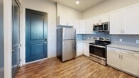 Located at 532 W Colorado Ave in Colorado Springs, Colorado, this single-floor unit offers a clean, modern aesthetic with thoughtfully selected finishes throughout. The kitchen serves as a functional centerpiece, showcasing white shaker-style cabinetry, granite countertops, a light blue subway tile backsplash, and a full suite of stainless steel appliances including a refrigerator, electric range, and over-the-range microwave. Wood-look flooring runs through the kitchen and connects seamlessly to the adjacent areas, lending warmth and continuity to the open layout. The bathroom continues the refined design language with white cabinetry, granite countertops, a large vanity mirror, and recessed lighting, creating a clean and functional space. The bedroom features plush carpeting, a ceiling fan, and multiple windows dressed with horizontal blinds that allow for ample natural light while maintaining privacy. The unit's neutral color palette of soft whites and warm grays provides a versatile backdrop throughout. A bold navy blue entry door adds a distinctive accent upon arrival. The 3D dollhouse view reveals a compact yet efficiently arranged floor plan, with the kitchen, bathroom, and bedroom logically connected for ease of living.