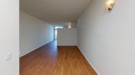 Located at 8503 Tobias Ave in the Panorama City neighborhood of Los Angeles, this single-floor unit offers a clean, functional layout with a bright and open feel throughout. The main living area is generously proportioned, showcasing warm-toned hardwood flooring that extends across the entirety of the space. White walls and a textured ceiling keep the aesthetic light and airy, while a skylight positioned near the transition to the kitchen allows natural light to pour into the heart of the unit. A half-wall pass-through counter separates the living area from the kitchen, creating an open yet defined division between the two spaces. The kitchen is compact and efficiently arranged, featuring standard appliances and cabinetry. The bathroom is thoughtfully appointed with a wide vanity topped by a large wall-spanning mirror, white cabinetry offering ample storage below, and chrome fixtures. A separate water closet provides added privacy. The overall design is understated and practical, with a neutral color palette of whites and warm wood tones creating a cohesive and welcoming ambiance throughout the unit.