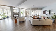 Located at 1001 Bolling Ave in Norfolk, Virginia, this single-floor community amenity space offers a well-appointed and thoughtfully designed environment for gathering, working, and relaxing. The expansive open-plan lounge area serves as the centerpiece of the space, featuring wide-plank hardwood-style flooring, neutral tones, and a striking double-sided linear fireplace that anchors the room while allowing sightlines through to the sun-filled lounge beyond. Large floor-to-ceiling windows and glass doors flood the interior with natural light and provide views of the surrounding greenery, enhancing the open and airy atmosphere. Comfortable seating arrangements, including generous sofas and accent chairs, are thoughtfully arranged throughout the lounge to accommodate both social interaction and quiet relaxation. A fully equipped kitchen features rich dark cabinetry, granite countertops, a tiled backsplash, stainless steel appliances including a refrigerator, dishwasher, and microwave, as well as open shelving for convenient storage. Dedicated workspace areas include a granite-topped desk station with computer access, a glass board, and a private workspace room with frosted glass door access, catering to productivity needs. Interior glass partitions add visual connectivity between zones while maintaining defined areas, creating a cohesive and functional community hub.