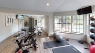Located at 4155 Satellite Blvd in Duluth, Georgia, this well-appointed fitness center offers a comprehensive workout environment designed to support a wide range of exercise routines. The single-floor facility features light-toned hardwood-style flooring and neutral gray walls, creating a clean, modern aesthetic throughout.

The cardio zone is equipped with treadmills, an elliptical trainer, and a stationary cycling bike, all positioned to take advantage of the natural light that streams in through large multi-pane windows. French-style glass doors provide additional brightness and direct access to the outdoors. A colorful geometric wall accent adds a vibrant focal point to this section of the room.

The strength training area includes a cable machine, weight bench, and various resistance equipment, complemented by floor-to-ceiling mirrors that enhance the sense of space. Stability balls and exercise mats are available for stretching and functional fitness. A dedicated free-weight station features an organized rack of kettlebells in multiple sizes and colors, catering to varied training needs.

Recessed lighting throughout ensures consistent illumination during all hours. A water dispenser is conveniently situated within the space, and a separate door provides access to an additional room. The facility is rounded out with a bench seating area and motivational wall art, contributing to an energetic yet focused atmosphere.