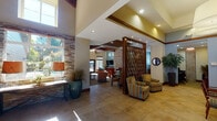 Located at 22435 SE 240th St in Maple Valley, Washington, this single-floor space is thoughtfully designed with a warm, lodge-inspired aesthetic that blends natural materials with modern comfort. The welcoming entry area features soaring vaulted ceilings with exposed wood beam detailing, large-format tile flooring, and striking stacked stone accent walls that establish a refined yet inviting atmosphere throughout.

The main lounge area is generously proportioned, anchored by rich wood ceiling beams and flooded with natural light through large windows and glass doors that open to an outdoor pool area. A stacked stone fireplace wall serves as a dramatic focal point, complemented by a wall-mounted television and built-in shelving. Comfortable seating arrangements, including a large sectional sofa and accent chairs in warm tones, make this area ideal for gathering and relaxation.

An artisan-crafted kitchen island with butcher block and stone countertops anchors the kitchen space, which is equipped with stainless steel appliances, rich wood cabinetry, granite countertops, and a classic tile backsplash. A secondary kitchen alcove provides additional prep and storage space with ample cabinetry, a double basin sink, and a garden window with lush outdoor views.

Throughout the space, decorative wood screens, recessed lighting, and carefully curated décor contribute to a cohesive and polished design that balances warmth with elegance.