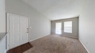 This single-story residence offers a clean, neutral aesthetic throughout, with soft carpet flooring across the main living and bedroom areas and durable hardwood-style flooring in the kitchen and bathroom. The living room is a standout space, featuring vaulted ceilings that lend an open, airy feel, along with a rear door and adjacent window that together invite ample natural light into the room. The layout flows naturally from the entryway through the living space and into the rest of the home. The kitchen is efficiently designed, offering granite-style countertops, light wood cabinetry, and black appliances including an electric range and refrigerator. A dedicated utility area is accessible just off the kitchen. The bedroom is comfortably sized, with a ceiling fan, a broad window for natural light, and soft carpeting underfoot. The bathroom features a full-size tub and shower combination with white tile surround, complemented by hardwood-style flooring. Throughout the home, neutral gray walls, white trim, and textured ceilings create a cohesive and understated palette that provides a versatile backdrop for any interior style.
