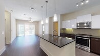 Located at 8255 Walnut Hill Lane in Dallas, Texas, this single-floor residence offers a contemporary design with a cohesive aesthetic throughout. The open-concept kitchen serves as the centerpiece, anchored by a substantial island topped with dark granite countertops and fitted with an undermount sink and modern pendant lighting. White upper cabinetry contrasts sharply with dark lower cabinets, complemented by a tile backsplash and a full suite of stainless steel appliances, including a range, microwave, and refrigerator. Track lighting and recessed fixtures illuminate the space effectively.

The kitchen flows seamlessly into a generously sized living area featuring dark hardwood-style flooring, a ceiling fan, and sliding glass doors that open to an outdoor balcony or patio, allowing natural light to fill the space. Bedrooms are well-proportioned with windows fitted with blinds, ceiling fans, and neutral walls. The primary bathroom includes a glass-enclosed shower, a soaking tub, dark granite vanity, and direct access to a walk-in closet outfitted with wire shelving systems. A secondary bathroom mirrors the modern finishes seen throughout the unit.