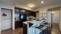 Located at 3995 S. Hamilton Rd. in Groveport, Ohio, this single-floor residential unit offers a thoughtfully designed layout with modern finishes throughout. The kitchen serves as a centerpiece of the home, showcasing rich dark espresso cabinetry that extends to the ceiling for ample storage, light granite countertops, and black appliances including a refrigerator, range, and built-in microwave. A spacious island with a built-in sink and breakfast bar seating provides both additional prep space and a casual dining area. Wood-style plank flooring runs throughout the kitchen and living areas, adding warmth and continuity to the open layout. The living area offers a comfortable, carpeted space with neutral tones. The bedrooms are carpeted and feature natural light from windows with blinds and curtain treatments, along with generous closet space. The bathrooms are well-finished, with one featuring a sleek glass-door walk-in shower and granite vanity countertop, while another offers tile flooring and clean, neutral walls. Throughout the unit, a consistent neutral color palette and textured ceilings create a cohesive, move-in-ready atmosphere suited for everyday living.