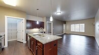 This well-appointed 2-bedroom, 2-bathroom residence in West Fargo, North Dakota offers a thoughtfully designed single-floor layout with a seamless blend of style and functionality. The open-concept kitchen and living area serves as the heart of the home, anchored by a central island with a granite countertop, double sink, and pendant lighting. Rich dark cabinetry, stainless steel appliances—including a range, microwave, and dishwasher—and a separate pantry make the kitchen both practical and visually striking. Wood-style flooring flows throughout the main living areas, while a private entrance door with a sidelight window brings in natural light. Both bedrooms feature plush carpeting and windows that allow natural light to fill the rooms. The primary bedroom connects directly to its own bathroom, which is finished with a granite-topped vanity, rich cabinetry, and a full soaking tub. The second bathroom mirrors this quality with matching finishes. A dedicated laundry room houses a full-size washer and dryer. Generous closet space, including a spacious walk-in closet with wire shelving, adds to the home's practicality. Neutral tones throughout create a clean, move-in-ready aesthetic.