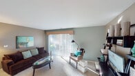 This single-floor residence offers a thoughtfully designed layout that balances comfort and functionality throughout. The living room is bright and welcoming, featuring plush carpeting, soft teal accent walls, and a large sliding glass door framed by vertical blinds that floods the space with natural light and provides outdoor access. A dedicated media and shelving area adds practical storage and display options to the room.

The galley-style kitchen is efficiently organized with light wood cabinetry, speckled quartz countertops, stainless steel appliances including a range and refrigerator, a double-basin sink, and wood-look flooring. A skylight adds brightness to the workspace. Adjacent to the kitchen, a dedicated dining area features warm hardwood-style flooring, a statement pendant light, and a large window that brings in natural light.

The bedroom is generously proportioned with carpet flooring, a ceiling fan, and a window with exterior views. It connects directly to a spacious walk-in closet equipped with wire shelving and hanging rods, which in turn leads to a full en-suite bathroom. The bathroom features a wide vanity with a granite-style countertop, dual lighting fixtures, tile flooring, and a tub-shower combination. The overall palette of neutral tones accented with teal creates a cohesive, modern aesthetic throughout the space.