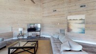 Located at 2525 Center West Pkwy in Augusta, Georgia, this single-floor community space showcases a warm, rustic aesthetic defined by light-toned shiplap wood paneling that lines the walls throughout. Soaring vaulted ceilings with exposed beams and ceiling fans amplify the sense of openness, while durable wood-look flooring grounds the interior with a cohesive, natural feel.

The main living area is generously proportioned, offering multiple seating arrangements including tufted sofas, leather armchairs, and glass-top coffee tables, making it well-suited for both relaxed gatherings and casual meetings. A large flat-screen television is mounted on a media stand in the corner, complemented by framed artwork that adds a refined touch to the rustic backdrop.

A dedicated workstation area features built-in cabinetry with a dark countertop and computer equipment, providing a functional workspace within the same open footprint.

The dining area is a standout feature, bathed in abundant natural light streaming through a sweeping wall of large windows and French doors. These openings frame direct views of an outdoor pool and lush landscaping, creating a seamless connection between the interior and exterior. Exposed ceiling beams arch overhead in this zone, reinforcing the architectural character of the space.

Overall, the space balances rustic charm with practical amenities, offering a welcoming and versatile environment.