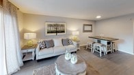 This single-floor residence is thoughtfully laid out to maximize functionality across its living spaces. The open floor plan, visible in the overhead view, positions the kitchen and living area in a connected configuration, promoting ease of movement throughout the common areas.

The kitchen features a galley-style design with rich dark cabinetry, granite-look countertops, a stainless steel sink, and black appliances including a refrigerator and range. Light-toned tile flooring completes the clean, practical aesthetic of this space.

The living room offers a welcoming atmosphere with neutral gray walls, wood-look flooring, and recessed lighting. The space is well-proportioned and accommodates both a seating and dining area comfortably.

Multiple bedrooms are present, each carpeted and finished with neutral gray walls. The rooms receive natural light through windows dressed with curtains and blinds. Closet access is available in at least one bedroom.

Two full bathrooms feature tub-shower combinations, dark vanity cabinetry, white countertops, large mirrors, and neutral tile flooring, providing a clean and functional finish throughout. The overall design is consistent and cohesive across all rooms.