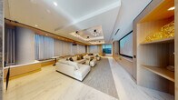 This elegantly designed single-floor space blends the functionality of a screening room with the comfort of an upscale lounge. The expansive main area is anchored by a large projection screen along one wall, flanked by built-in wood cabinetry and media storage. Plush, cream-toned sectional sofas and modular seating arrangements are positioned across a textured area rug atop polished marble-look flooring, creating multiple conversation and viewing zones. A tiered bench seating area with warm wood detailing lines one wall, adding a theater-inspired element.

The coffered ceiling features dramatic, branch-like sculptural chandeliers paired with recessed lighting, lending both warmth and visual interest. Floor-to-ceiling sheer drapery diffuses natural light throughout the space, while a corner window offers outdoor views of the surrounding urban environment.

A separate wet bar area is equipped with under-counter refrigeration, a sink, and pendant lighting suspended from a wood-paneled ceiling, providing convenient service for events. An adjoining conference area offers a substantial marble-topped table set before expansive floor-to-ceiling windows with sweeping city views, completing this versatile, refined environment.