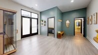 Located at 1000 Washington Ave in St. Louis, Missouri, this thoughtfully designed single-floor space offers a clean, modern aesthetic across two rooms and two bathrooms. The main open area greets visitors with light gray luxury vinyl plank flooring, recessed lighting, and striking sage-green accent walls that lend a calm, contemporary feel. Large black-framed glass double doors flood the space with natural light, creating an airy and welcoming atmosphere. A decorative wall-mounted mirror with an organic silhouette, floating shelves with greenery, and a wooden bench add warmth and personality to the entryway area. A hallway lined with dark-trimmed doors connects the main room to the secondary space, which features crisp white walls, recessed lighting, and a wooden console table flanked by framed botanical and abstract artwork — ideal for display or functional use. The two bathrooms are cleanly finished, with one showcasing subway tile detailing and a dark vanity, while the other offers a minimalist design with wood-toned flooring and simple, functional fixtures. Throughout the space, dark door frames and hardware provide a modern contrast against neutral walls, creating a cohesive and polished interior. The overall ambiance is calm, curated, and well-suited for a variety of uses.