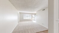 Located at 550 Los Arbolitos Boulevard in Oceanside, California, this single-floor, 3-bedroom, 2-bathroom residence offers a functional and comfortable layout designed for everyday living. The open living and dining area is generously sized, featuring soft carpet flooring, neutral-toned walls, and a textured ceiling. Large windows and a sliding glass door flood the space with natural light while providing direct access to a private balcony — ideal for enjoying the sunny Southern California climate. The kitchen is positioned adjacent to the living area and features dark countertops, white cabinetry, and black appliances, with wood-style flooring that extends into the dining space. Three well-proportioned bedrooms each offer carpeted floors, windows with blinds, and access to closets, with the primary bedroom providing a notably spacious retreat. Both bathrooms are finished in clean white tiling and include a shower-tub combination with wood-style flooring. A hallway connects the private areas of the home, and three closets throughout the unit provide ample storage. The exterior showcases a low-profile roofline, a wood-paneled balcony, and mature palm and pine trees that complement the relaxed Oceanside surroundings.