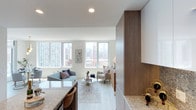 This thoughtfully designed single-floor residence offers a bright, open-concept layout with sweeping city skyline views visible from multiple rooms. Large floor-to-ceiling and oversized windows flood the living and dining areas with natural light, framing dramatic urban vistas. The living room comfortably accommodates a seating arrangement anchored by light wood-style flooring that extends throughout the unit.

The kitchen is a standout feature, showcasing granite countertops, a full granite backsplash, dual-tone cabinetry combining walnut wood and high-gloss white upper cabinets, stainless steel appliances including a gas range and wall oven, and a generous island with seating. A dedicated dining area benefits from corner windows and is accented by a sculptural brass pendant light above a glass-top table.

The primary bedroom connects to a private balcony through glass doors, offering additional skyline views. A second bedroom features textured accent wallpaper and a sliding closet. The bathroom is finished with large-format tile, a soaking tub with shower, and a walnut vanity. A third flexible room with a stone accent wall provides versatile use. Recessed lighting and a neutral palette complete the refined, contemporary ambiance.