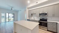 This well-designed single-floor residence offers a clean, contemporary aesthetic throughout, highlighted by light wood-tone flooring and a crisp white color palette that enhances the sense of openness and brightness.

The kitchen is a standout feature, showcasing grey shaker-style cabinetry with ample upper and lower storage, white quartz countertops, a classic white subway tile backsplash, and a full suite of stainless steel appliances including a double oven range, built-in microwave, dishwasher, and a French door refrigerator. A generous island provides additional counter space and serves as a natural gathering point, with the kitchen flowing seamlessly into the adjacent living area.

The bedrooms are bright and airy, each featuring light wood flooring, neutral white walls, and windows that bring in natural light with views of the surrounding exterior. Exposed ceiling beams add a subtle architectural detail to these rooms.

The bathrooms are finished in a clean, modern style. One features a full soaking tub with a tiled surround and chrome fixtures, while the other includes a glass-enclosed shower alongside a grey vanity with a white countertop. Both continue the light wood flooring found throughout the residence.

A dedicated laundry area houses a full-size top-loading washer and dryer. The hallway connecting the rooms is clean and uncluttered, reinforcing the home's open and functional layout.