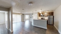 This single-floor unit is designed with an open, functional layout that connects the main living and kitchen areas seamlessly. Dark hardwood-style flooring runs consistently throughout the space, providing a cohesive and contemporary aesthetic. The living area is generously sized, featuring a ceiling fan with a light fixture and a large sliding glass door fitted with vertical blinds, allowing natural light to fill the room while offering access to an outdoor view.

The kitchen is positioned adjacent to the living space and is defined by a peninsula-style breakfast bar. It is equipped with stainless steel appliances, including an electric range, microwave, and refrigerator. Dark cabinetry with ample storage pairs with light quartz-style countertops and a white subway tile backsplash, creating a well-balanced contrast. Pendant lighting and a track light fixture illuminate the kitchen effectively.

Two bedrooms are each appointed with ceiling fans, closet storage, and windows that bring in natural light. Both bathrooms follow a consistent design language, featuring light large-format tile surrounds in the tub-shower combinations, dark vanity cabinetry, quartz-style countertops with undermount sinks, and framed mirrors. Textured ceilings and clean white baseboards are present throughout the unit.