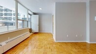 This 2-bedroom, 2-bathroom residence is laid out across a single floor, offering a functional and comfortable living arrangement. Warm parquet wood flooring is a defining feature throughout the main living areas and both bedrooms, lending a classic, timeless character to the space. The living room is generously proportioned, filled with natural light from large windows, and equipped with baseboard heating, creating a bright and inviting atmosphere. A hallway connects the main living areas to the private quarters, providing a clear and logical flow throughout the unit. Both bedrooms are well-sized, each featuring sliding-door closets for ample storage and the same rich parquet flooring. The primary bedroom offers additional space and a window that brings in natural light. The kitchen has been updated with clean white cabinetry, white quartz countertops, a stainless steel undermount sink with a modern pull-down faucet, a white subway tile backsplash, and stainless steel appliances, including a dishwasher. The two bathrooms are finished with white rectangular wall tiles, a soaking tub with shower, a white vanity, and light tile flooring, presenting a clean and cohesive aesthetic. A textured ceiling is present in select areas of the unit.