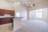 This single-floor residence is defined by its open-concept layout and impressive vaulted ceilings that lend an expansive, airy feel to the main living area. The kitchen is a standout feature, showcasing rich cherry wood cabinetry, dark granite countertops, and a full suite of black appliances including a refrigerator, electric range, built-in microwave, and dishwasher. Tile flooring runs throughout the kitchen, and a central peninsula with a dark countertop provides additional workspace while naturally connecting the kitchen to the adjacent living area. A ceiling fan with pendant lighting serves the combined living and dining space, enhancing both comfort and ambiance. The bedrooms are generously proportioned, finished with soft wall-to-wall carpeting and neutral tones that create a calm, welcoming atmosphere. One bedroom includes access to a closet with built-in shelving. Large windows allow natural light to filter into the living and bedroom spaces, offering views of the surrounding greenery. The bathrooms are finished with the same cherry cabinetry and granite countertops found in the kitchen, complemented by tile flooring, a single undermount sink, and a shower-tub combination. Grab bars in the bathrooms add a practical, accessible touch throughout this well-appointed residence.