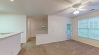 Located at 916 Sugar Gap Rd in Wake Forest, NC, this single-floor home offers a clean, functional layout designed for comfortable everyday living. The open living area is finished with plush carpeting and features a ceiling fan with light fixture, a rear exterior door with a glass panel that allows natural light to filter in, and a large window that frames views of surrounding greenery. A half-wall partition visually separates the living space from the kitchen, where a pendant light adds a warm accent. The kitchen is well-appointed with warm-toned wood cabinetry, white appliances including a range, built-in microwave, dishwasher, and refrigerator, a double-basin sink, and light-toned countertops. Hardwood-style flooring runs throughout the kitchen, adding a welcoming contrast to the carpeted living and bedroom areas. A doorway from the kitchen leads to an additional utility or pantry space. The bedroom is generously sized, carpeted, and equipped with a ceiling fan and a bright window overlooking the outdoors. The bathroom features hardwood-style flooring, a wood-toned vanity with a large mirror, a single-basin sink with ample counter space, and a full tub-shower combination. The overall aesthetic is clean, neutral, and move-in ready.