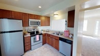 This two-floor space includes a thoughtfully designed kitchen that serves as a functional centerpiece. The kitchen is laid out in an efficient L-shape configuration, maximizing the use of available space. Rich, warm-toned wood cabinetry lines the walls both above and below the countertops, providing generous storage throughout. The countertops feature a granite-style surface that complements the cabinetry's warm tones. Stainless steel appliances, including an electric range with matching over-the-range microwave, a double-basin sink, and a dishwasher, lend a modern and cohesive aesthetic to the kitchen. Recessed and flush-mount ceiling lighting ensures the space is well-lit and practical. The light-toned flooring adds brightness to the kitchen, creating a clean and inviting atmosphere. The kitchen's design reflects attention to both form and function, with ample counter space for meal preparation. Being spread across two floors, this space offers distinct zones for living and other activities, enhancing overall functionality.