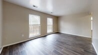 This single-story residence at 1800 Boydton Plank Rd in Petersburg, Virginia offers a practical and well-organized layout across one level. The living and common areas are finished with dark hardwood-style flooring, lending a clean, contemporary feel to the space. Multiple windows throughout the home invite natural light and offer views of the surrounding greenery, creating a bright and welcoming atmosphere.

The galley-style kitchen is efficiently designed, featuring white cabinetry, white appliances including a gas range, microwave, and refrigerator, all set atop light hardwood-style flooring. A door at the end of the kitchen provides convenient access to the exterior.

The multiple bedrooms are finished with plush, neutral-toned carpet, providing a comfortable and quiet environment. Each bedroom includes a window with outdoor views, and several rooms feature closets with built-in shelving for ample storage. The primary bedroom is notably spacious and includes two closets.

The bathroom is cleanly appointed with a white vanity, a lighted mirror, a tub-shower combination, and durable wood-look flooring. Neutral wall tones are consistent throughout the home, contributing to a cohesive and understated aesthetic well-suited for a variety of interior styles.