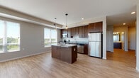 This single-floor residence offers a thoughtfully designed open-concept layout finished with contemporary details throughout. The kitchen serves as a central highlight, featuring rich dark-stained cabinetry, granite countertops, a substantial center island with pendant lighting, a classic white subway tile backsplash, and a full suite of stainless steel appliances. Large windows flood the kitchen and adjacent living area with abundant natural light while offering outdoor views of the surrounding landscape.

Light-toned hardwood-style flooring runs throughout the main living areas, creating a clean, cohesive look that extends into the bright hallways and open living space. A glass-paneled exterior door in the living area provides access to an outdoor balcony and further enhances the sense of openness and connection to the outdoors.

The bedrooms provide a comfortable retreat, with plush carpeting underfoot and windows that continue to bring in natural light. The bathrooms are finished with matching dark cabinetry, white countertops, and light flooring. Accessibility-conscious grab bars are installed in the bathrooms, reflecting thoughtful, inclusive design.

Neutral tones in warm beige and soft gray carry throughout the space, contributing to a calm and welcoming ambiance. The overall layout flows efficiently, making this a well-appointed and functional residence.