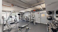 This 620 square foot gym, located in Miami, FL, is a single-floor facility designed for comprehensive fitness training. The space features an industrial-style exposed ceiling with visible ductwork and pipes, creating a modern urban aesthetic. Bright LED lighting fixtures illuminate the area effectively.

The gym is equipped with a wide range of exercise machines and equipment. Cardio enthusiasts will find multiple treadmills and elliptical machines, strategically placed near large windows that offer natural light and street views. For strength training, the facility includes various weight machines, free weights, and benches.

The floor is covered with durable, dark gray rubber matting, ideal for heavy equipment and intense workouts. White and light gray walls contribute to a clean, bright atmosphere. Wall-mounted TVs and speakers are installed for entertainment and motivation during exercise sessions.

Notable features include a dedicated area for stretching and floor exercises, well-organized equipment placement for easy navigation, and ample space between machines for comfort and safety. The gym also incorporates modern amenities such as water stations and sanitizing areas.

Overall, this gym provides a comprehensive fitness environment in a compact, efficiently designed space, catering to various workout preferences and fitness levels.