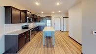 This single-floor unit offers a thoughtfully designed open-concept layout, seamlessly connecting the kitchen and living areas for a functional and cohesive feel. The kitchen is a standout feature, equipped with rich dark-stained cabinetry, stainless steel appliances including a range, microwave, dishwasher, and refrigerator, as well as granite countertops and a subway tile backsplash. A freestanding island with a light-colored top and blue base provides additional workspace and a casual gathering point. Light hardwood-style flooring runs throughout the main living areas, lending warmth and continuity to the space. The open living area is generously proportioned and filled with natural light from large windows that offer pleasant outdoor views. The bedrooms feature plush wall-to-wall carpeting, ceiling fans, and ample natural light, creating comfortable and restful retreats. The bathroom is well-finished with dark wood vanity cabinetry, granite countertops, a large mirror, and a full tub-shower combination, all set on wood-look flooring. Dark baseboards and trim provide a consistent, polished contrast throughout the unit, contributing to its modern and cohesive aesthetic.