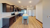 This single-floor unit offers a thoughtfully designed open-concept layout, seamlessly connecting the kitchen and living areas for a functional and cohesive feel. The kitchen is a standout feature, equipped with rich dark-stained cabinetry, stainless steel appliances including a range, microwave, dishwasher, and refrigerator, as well as granite countertops and a subway tile backsplash. A freestanding island with a light-colored top and blue base provides additional workspace and a casual gathering point. Light hardwood-style flooring runs throughout the main living areas, lending warmth and continuity to the space. The open living area is generously proportioned and filled with natural light from large windows that offer pleasant outdoor views. The bedrooms feature plush wall-to-wall carpeting, ceiling fans, and ample natural light, creating comfortable and restful retreats. The bathroom is well-finished with dark wood vanity cabinetry, granite countertops, a large mirror, and a full tub-shower combination, all set on wood-look flooring. Dark baseboards and trim provide a consistent, polished contrast throughout the unit, contributing to its modern and cohesive aesthetic.