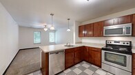 Located at 412 Welch Ave in Ames, Iowa, this two-bedroom, two-bathroom unit offers a practical and well-organized single-floor layout. The entry foyer features a classic grey-and-white checkered tile floor and provides immediate access to the main living areas, with clean white walls and modern panel doors throughout.

The kitchen is a functional highlight of the unit, outfitted with rich, warm-toned wood cabinetry, light countertops, and a full suite of stainless steel appliances including a range, over-the-range microwave, and refrigerator. The matching checkered tile flooring ties the kitchen to the entryway, creating a cohesive aesthetic.

Both bedrooms are carpeted and feature white walls, dark baseboards, and windows that allow natural light and views of the surrounding greenery. The primary bedroom is notably spacious, offering ample room for furnishings, and includes a ceiling fan for added comfort, along with access to a walk-in closet and an adjoining bathroom. The second bedroom also benefits from a window and dedicated overhead lighting.

The bathrooms echo the home's consistent design language, featuring checkered tile flooring, wood-toned vanities with light countertops, and well-lit mirrors. The layout as a whole is efficient and thoughtfully connected, making it a comfortable and functional living space.
