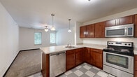 Located at 412 Welch Ave in Ames, Iowa, this two-bedroom, two-bathroom unit offers a practical and well-organized single-floor layout. The entry foyer features a classic grey-and-white checkered tile floor and provides immediate access to the main living areas, with clean white walls and modern panel doors throughout.

The kitchen is a functional highlight of the unit, outfitted with rich, warm-toned wood cabinetry, light countertops, and a full suite of stainless steel appliances including a range, over-the-range microwave, and refrigerator. The matching checkered tile flooring ties the kitchen to the entryway, creating a cohesive aesthetic.

Both bedrooms are carpeted and feature white walls, dark baseboards, and windows that allow natural light and views of the surrounding greenery. The primary bedroom is notably spacious, offering ample room for furnishings, and includes a ceiling fan for added comfort, along with access to a walk-in closet and an adjoining bathroom. The second bedroom also benefits from a window and dedicated overhead lighting.

The bathrooms echo the home's consistent design language, featuring checkered tile flooring, wood-toned vanities with light countertops, and well-lit mirrors. The layout as a whole is efficient and thoughtfully connected, making it a comfortable and functional living space.