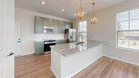 Located at 6899 Harlem Rd in Westerville, OH, this thoughtfully designed single-floor unit offers 1 bedroom and 1 bathroom within a compact yet efficient layout. The open-concept kitchen and living area serves as the heart of the home, featuring sage green shaker-style cabinetry with brushed gold hardware, granite countertops, a white subway tile backsplash, and a large central island with a built-in sink and stainless steel dishwasher. A stainless steel range and refrigerator complete the kitchen, while two geometric brass pendant lights add a modern, upscale touch. Multiple windows flood the space with natural light throughout. The living area flows seamlessly from the kitchen, benefiting from warm luxury vinyl plank flooring found throughout the unit. The bedroom is a quiet retreat featuring an elegant wainscoting accent wall, a large window with natural light, and direct access to a walk-in closet outfitted with wire shelving for ample storage. The bathroom continues the cohesive design with a green vanity, granite countertop, gold fixtures, and marble-look tile flooring. Additional conveniences include a dedicated laundry area and utility room, rounding out this efficiently designed, modern living space.