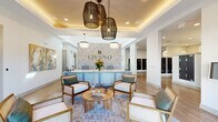 Located at 12020 Brush Hill Rd in Wildwood, Florida, this single-story community clubhouse for Livano Wildwood offers a thoughtfully designed gathering space that blends modern coastal aesthetics with functional amenities. The entrance greets visitors with a well-appointed reception area featuring the Livano branded front desk, set against a botanical-patterned accent wall, elegant woven pendant lighting, and a coffered ceiling with warm ambient lighting. Comfortable cane-back lounge chairs and a round wood coffee table create an inviting seating arrangement near glass French doors that frame views of the surrounding community. The expansive lounge and living area flows seamlessly from the entry, showcasing herringbone-patterned wood-look tile flooring throughout. Soaring ceilings with exposed beams and an abundance of natural light from tall windows lend an airy, open feel to the space. A cozy seating vignette anchors a sleek fireplace, while additional lounge groupings accommodate a variety of social settings. The dining area connects naturally to the lounge, offering casual seating for residents. A dedicated mailroom with rows of individual lockboxes provides practical, organized package and mail access. The overall ambiance is bright, modern, and welcoming, reflecting a refined yet relaxed Florida lifestyle.