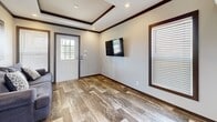 Located at 211 Benelli Dr in Hutto, TX, this efficiently designed single-story home offers two bedrooms and one bathroom within a thoughtfully arranged floor plan. Despite its compact footprint, the space maximizes every square foot through careful layout and consistent finishes.

The living area greets residents with a distinctive tray ceiling accented by dark wood trim, recessed lighting, and durable wood-look plank flooring that flows continuously throughout the home. Natural light enters through blinds-fitted windows, and a wall-mounted TV provides a functional focal point.

The kitchen features rich, dark wood cabinetry with brushed nickel hardware, light stone-look countertops, a stainless steel sink beneath a window, and black appliances including a range and refrigerator. A mini-split climate control unit in the living area ensures efficient temperature regulation.

The primary bedroom showcases a white shiplap accent wall, wall-mounted reading sconces, a built-in dark wood wardrobe, and its own mini-split unit. The second bedroom maintains the same cohesive aesthetic with coordinating cabinetry and natural light.

The bathroom includes wood-look tile flooring, a dark wood vanity with stone countertop, a shower with curtain, accessibility grab bars, and a small window for ventilation.