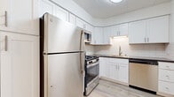 This 2-bedroom, 1-bathroom residence is thoughtfully laid out across a single floor, offering a clean and functional living environment with modern updates throughout. The kitchen is a standout feature, showcasing crisp white shaker cabinetry, classic subway tile backsplash, dark countertops, and a full suite of stainless steel appliances including a gas range, built-in microwave, dishwasher, and refrigerator. Light wood-style flooring ties the kitchen and living areas together seamlessly. The open living area is bright and airy, featuring light wood-style flooring, white walls, a ceiling fan, and a wall-unit air conditioner, with a window that brings in natural light and outdoor views of surrounding greenery. Both bedrooms are carpeted for comfort and feature louvered bi-fold closets, baseboard heating, and access to natural light through windows. The primary bedroom includes a wall-unit air conditioner and views of the neighborhood. The bathroom is finished with large-format tile flooring, a sleek white vanity with a mirrored medicine cabinet, and clean, bright fixtures. A hallway connects all rooms efficiently, and an additional closet provides extra storage. The space presents a cohesive, move-in-ready aesthetic throughout.