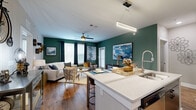 Located on Cheshire Bridge Road in Atlanta, GA, this single-floor residence offers a well-appointed, open-concept design that seamlessly connects the kitchen, dining, and living areas. The living room is immediately eye-catching, featuring bold deep-green accent walls, rich hardwood-style flooring, and a ceiling fan that adds both style and function. Natural light pours in through multiple windows dressed with elegant draping curtains, creating a warm and inviting atmosphere.

The kitchen is a standout feature, boasting a large central island with quartz countertops, a stainless steel undermount sink with a high-arc faucet, and a full suite of stainless steel appliances. Ample cabinetry provides generous storage, while the layout lends itself well to both everyday cooking and entertaining.

The primary bedroom offers a tranquil retreat with plush carpeting, a ceiling fan, and natural light filtering through blinds. The second bedroom mirrors this comfort with its own windows and ceiling fan. The bathroom is finished with wood-look tile flooring, a sleek vanity with an oversized mirror, and a glass-enclosed tiled shower.

A private balcony extends the living space outdoors, overlooking a lush, tree-lined landscape that provides a peaceful natural backdrop. This residence combines contemporary finishes with thoughtful design throughout.