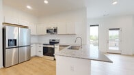 This single-floor unit presents a clean, contemporary design throughout, characterized by crisp white walls, light wood-tone flooring, and recessed lighting that contribute to a bright and airy atmosphere. The open-concept layout connects the kitchen and living area seamlessly, maximizing the sense of space and encouraging a natural flow between functional zones.

The kitchen is well-appointed with white shaker-style cabinetry extending to the ceiling, a white subway tile backsplash, and speckled granite countertops that carry through to a peninsula with an undermount stainless steel sink. A full suite of stainless steel appliances includes a French door refrigerator with ice and water dispenser, electric range, over-the-range microwave, and dishwasher. The living area benefits from large windows and a glass door that leads to an outdoor space, filling the interior with natural light.

The bedrooms are generously proportioned with white walls, the same light wood flooring, and ample closet space, including double-door closets. The bathroom features matching granite countertops on a white vanity with an undermount sink, gold-toned hardware accents, and a full tub-shower combination, maintaining the unit's cohesive modern aesthetic.